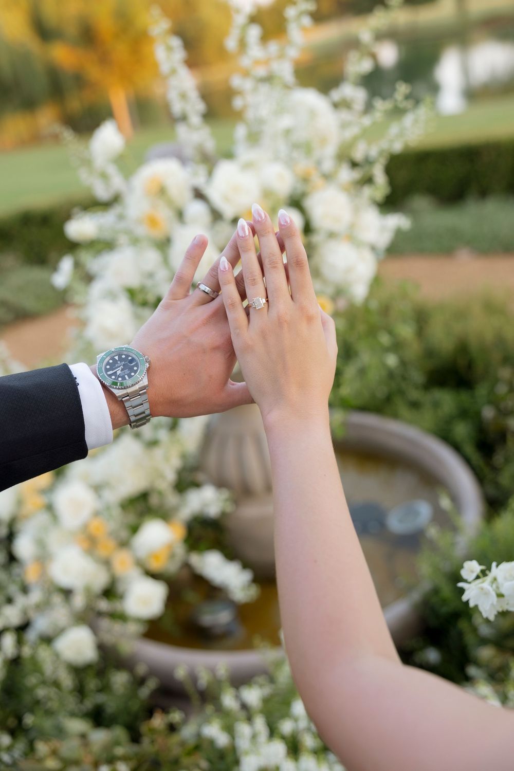 Close-up sequence showing hands exchanging wedding rings against a backdrop of white flowers.