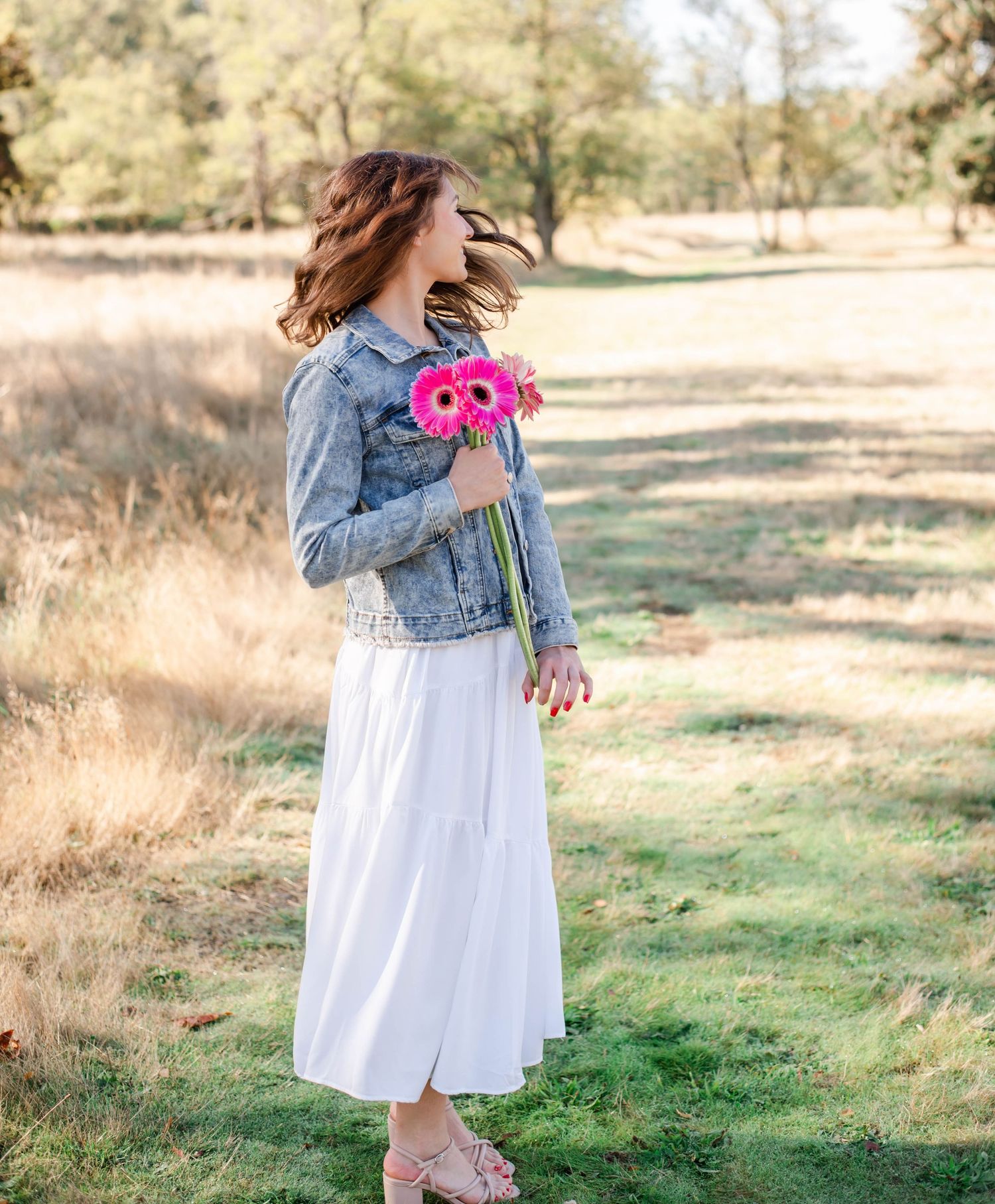 Person in white sweater and jeans lying on concrete wall with colorful flower bouquet creating artistic spring portrait.