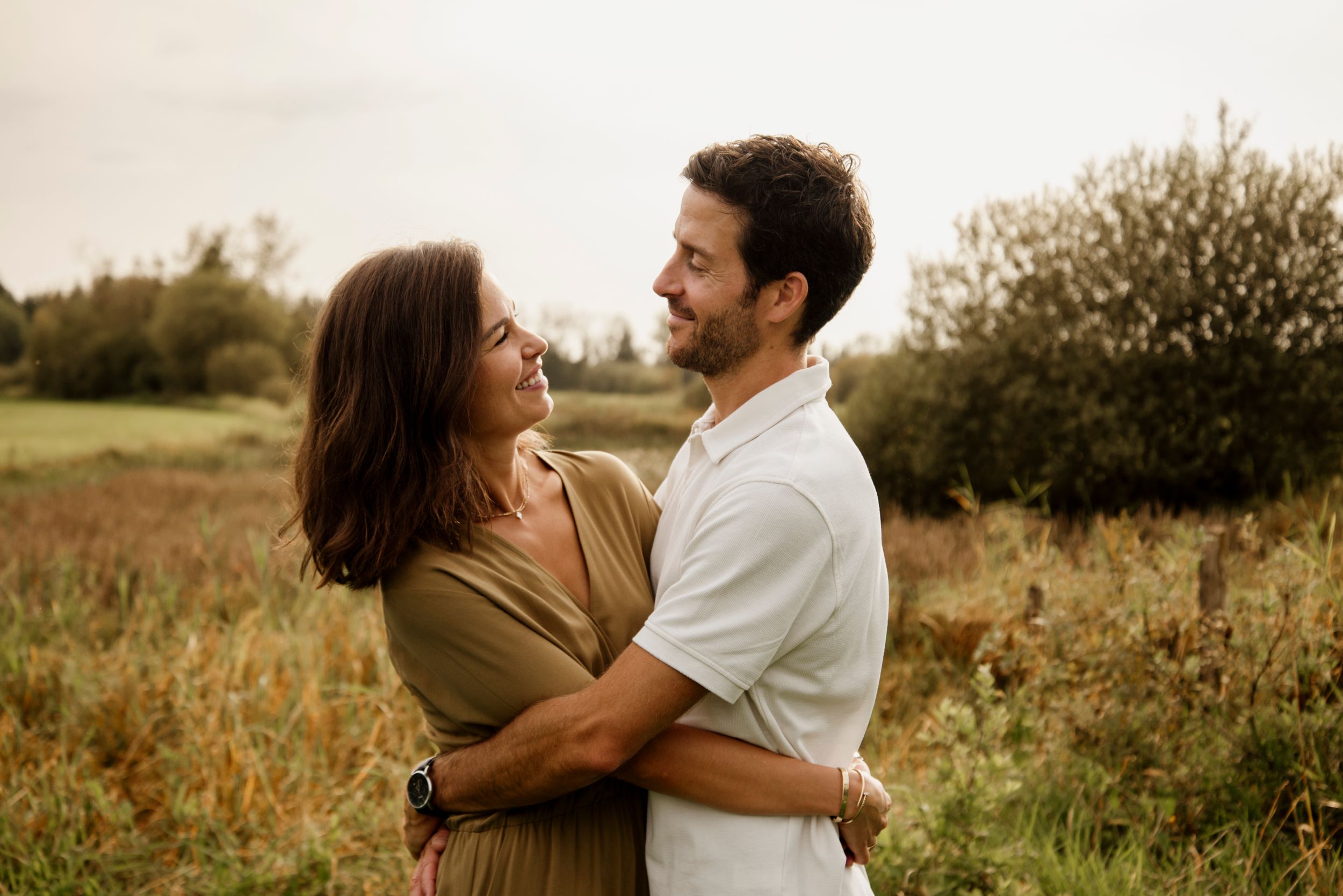 A couple embraces and gazes at each other lovingly in a lush outdoor field at golden hour.