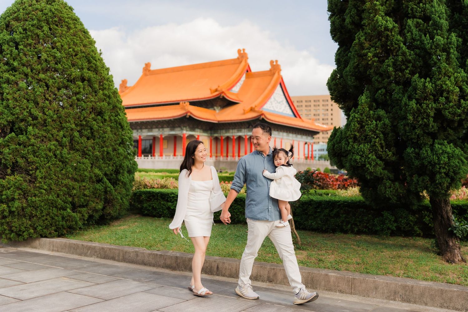 People practice Tai Chi exercises in a tranquil garden setting with traditional Asian architecture in the background.