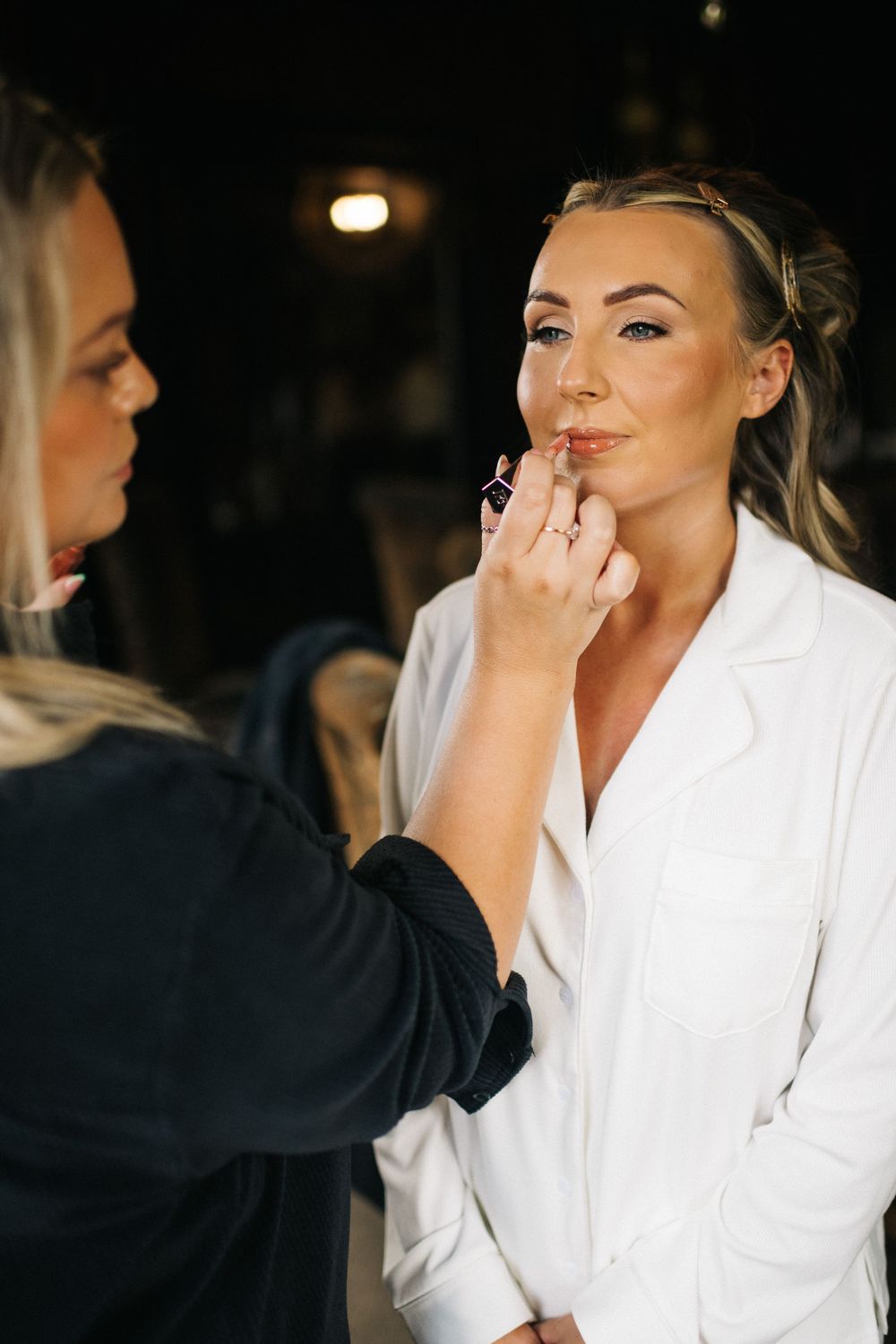Makeup artist applying lipstick to woman in white robe during wedding preparations.