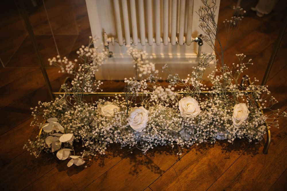 Delicate baby's breath and white floral arrangements decorate wooden floor at wedding venue.