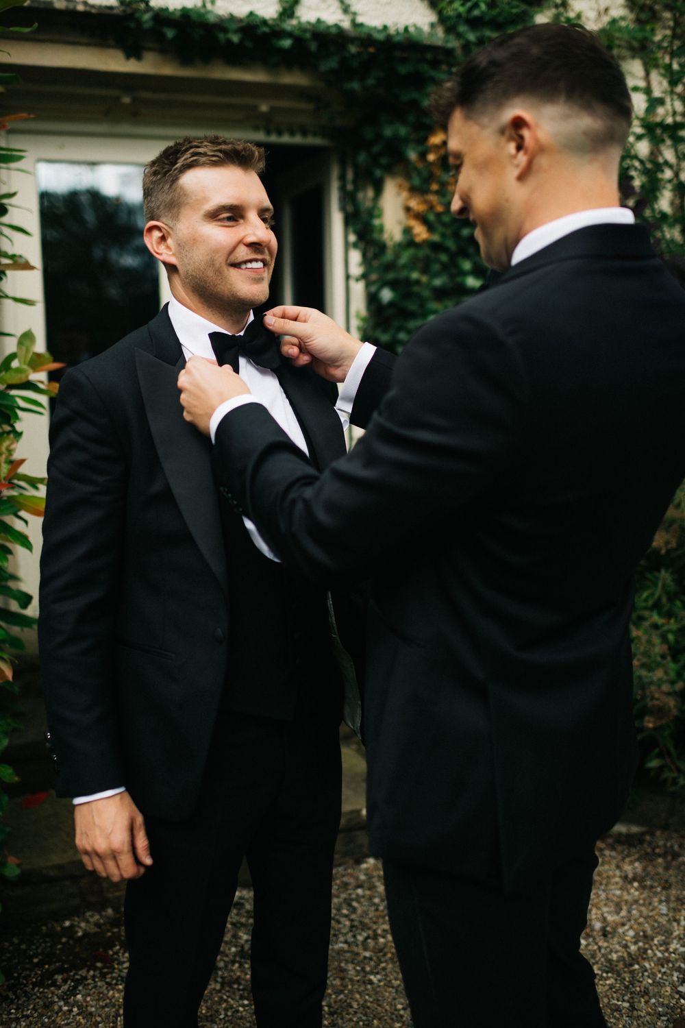 Groomsmen in black tuxedos helping each other adjust ties and boutonnieres before ceremony.