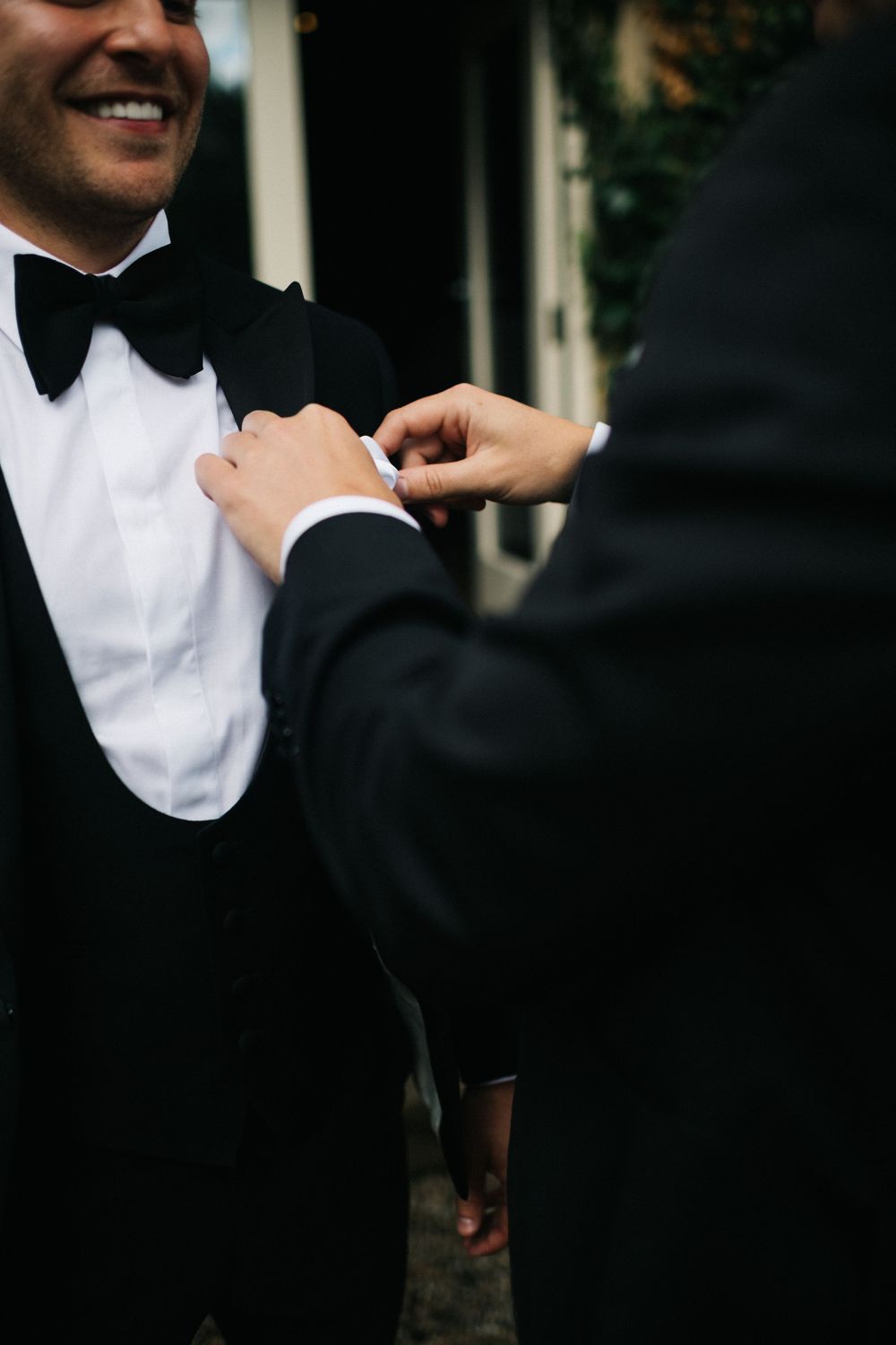 Close-up of someone adjusting a groom's black bow tie before the ceremony.