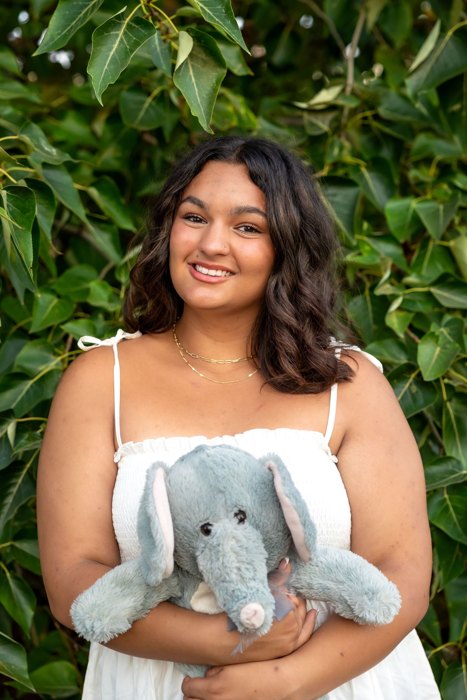 A series of outdoor portraits showing someone in a white top holding a plush elephant against a green leafy background.