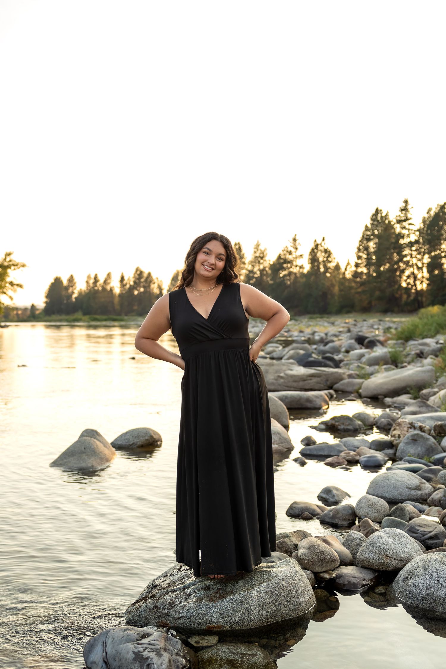 Sunset photoshoot at a rocky shoreline with water and golden light filtering through trees.
