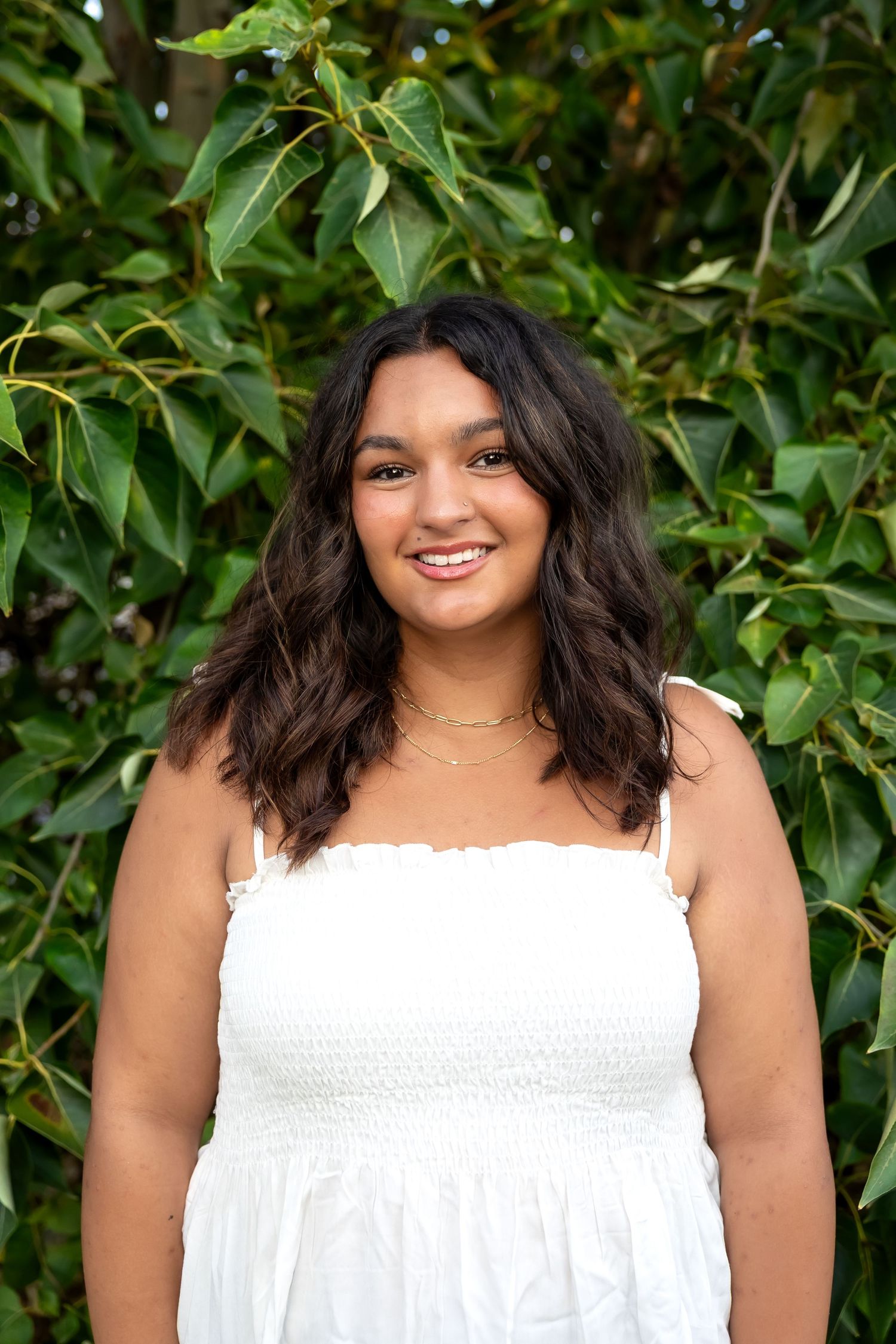 Outdoor portrait in a white summer top against lush green foliage background.