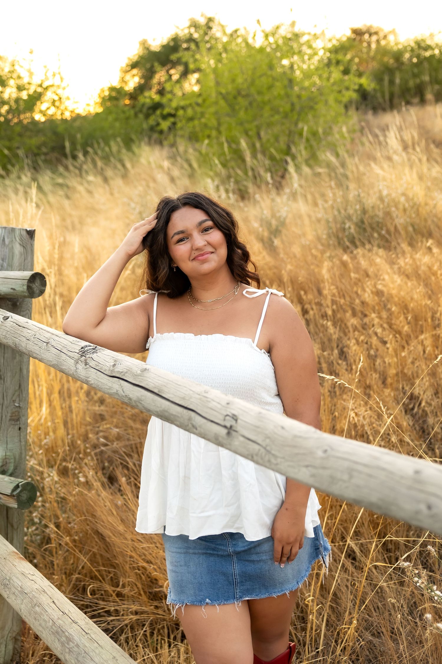 Summer portrait session in a golden field with rustic wooden fence during magic hour.