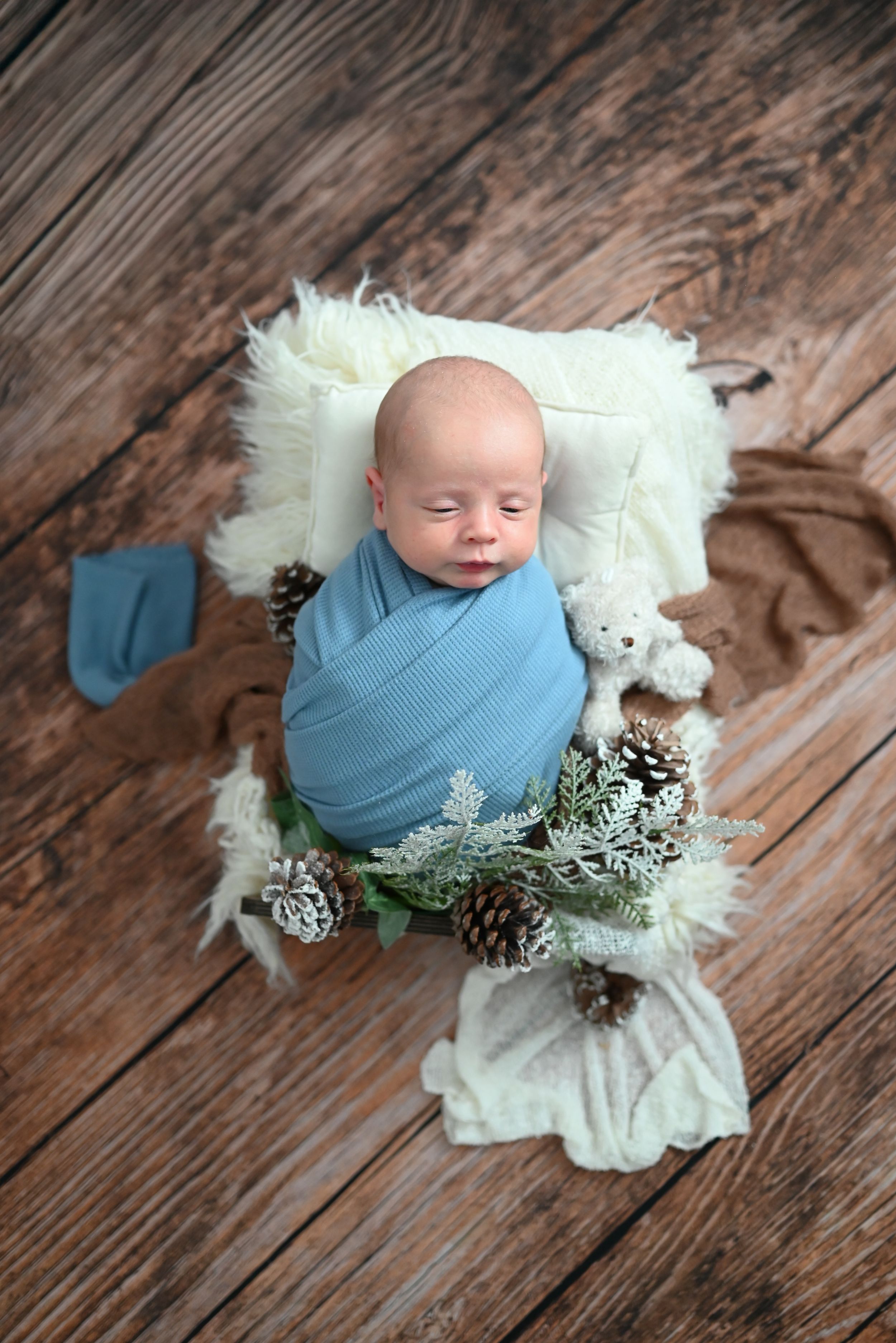 Newborn photography series showing baby wrapped in blue swaddle on white blanket with rustic wooden backdrop.