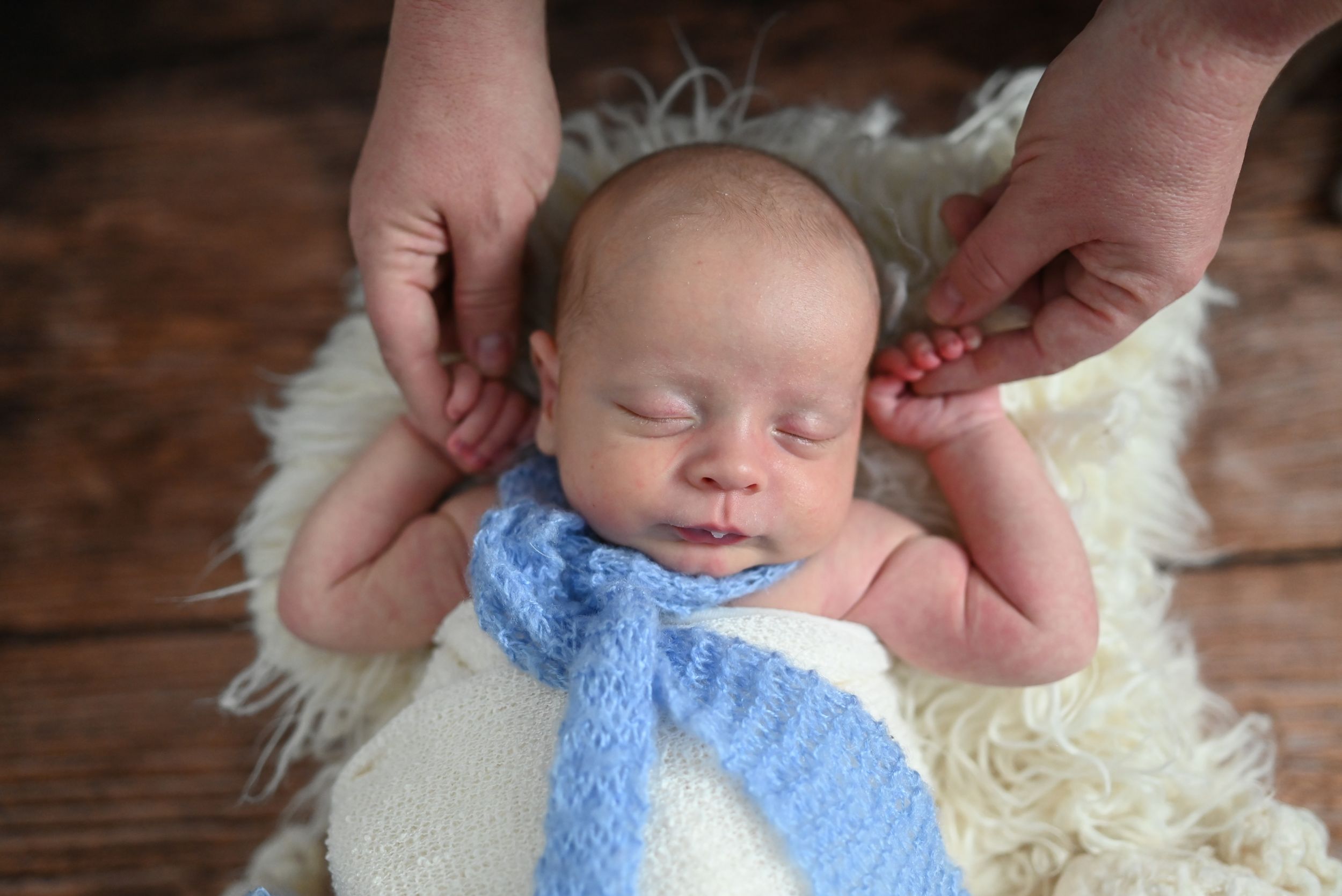A series of photos showing a newborn baby wearing a light blue knit hat being gently swaddled in a white blanket.