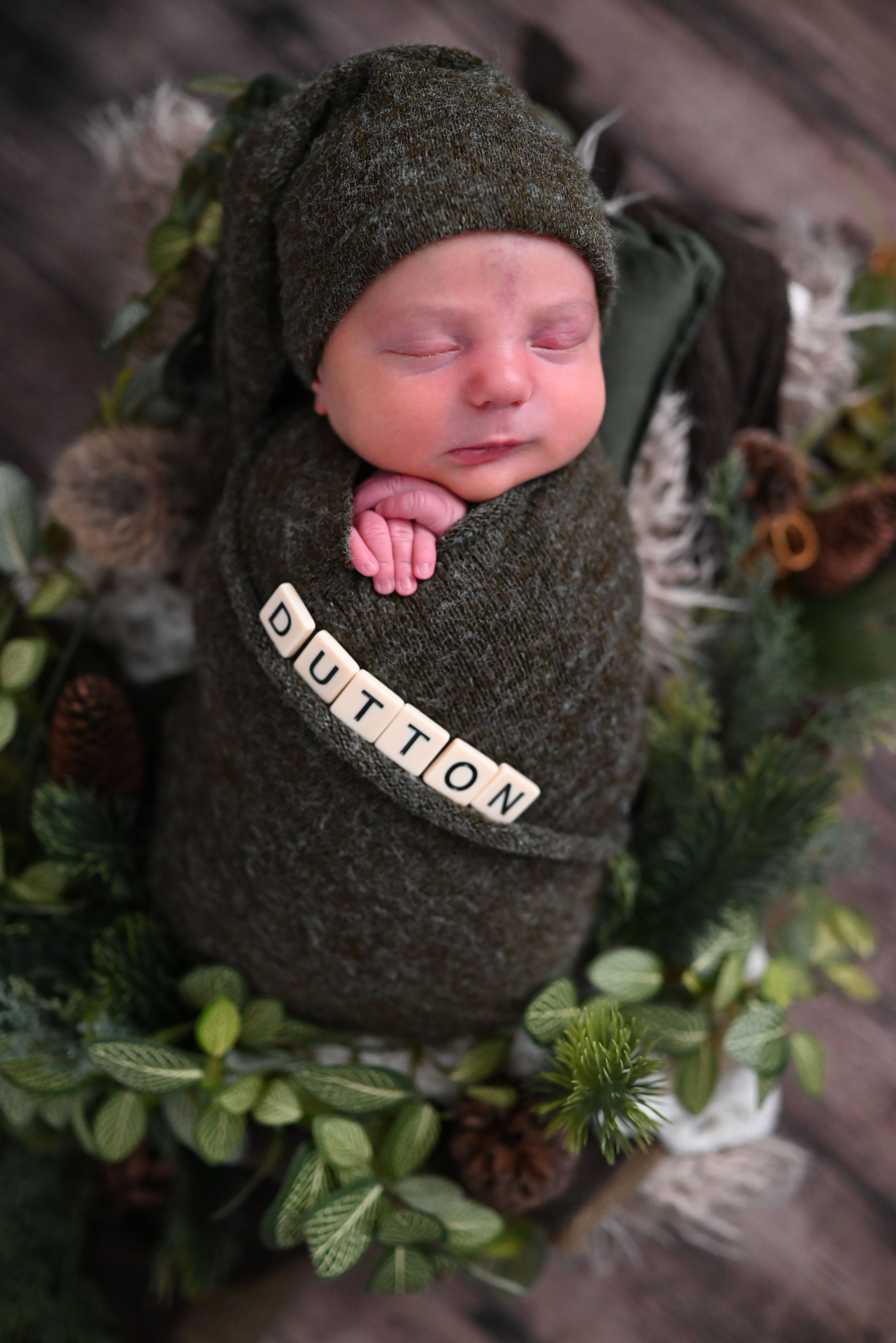 Newborn photography series with wooden letter blocks spelling DILLON amid cozy gray blankets and greenery decorations.
