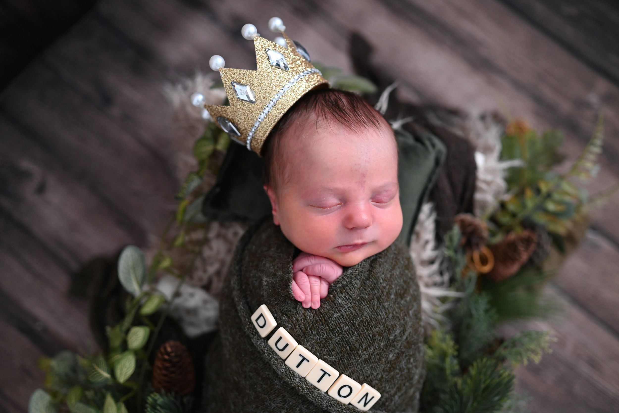 Newborn baby sleeps peacefully in soft grey wrap with delicate floral decorations around the edges.