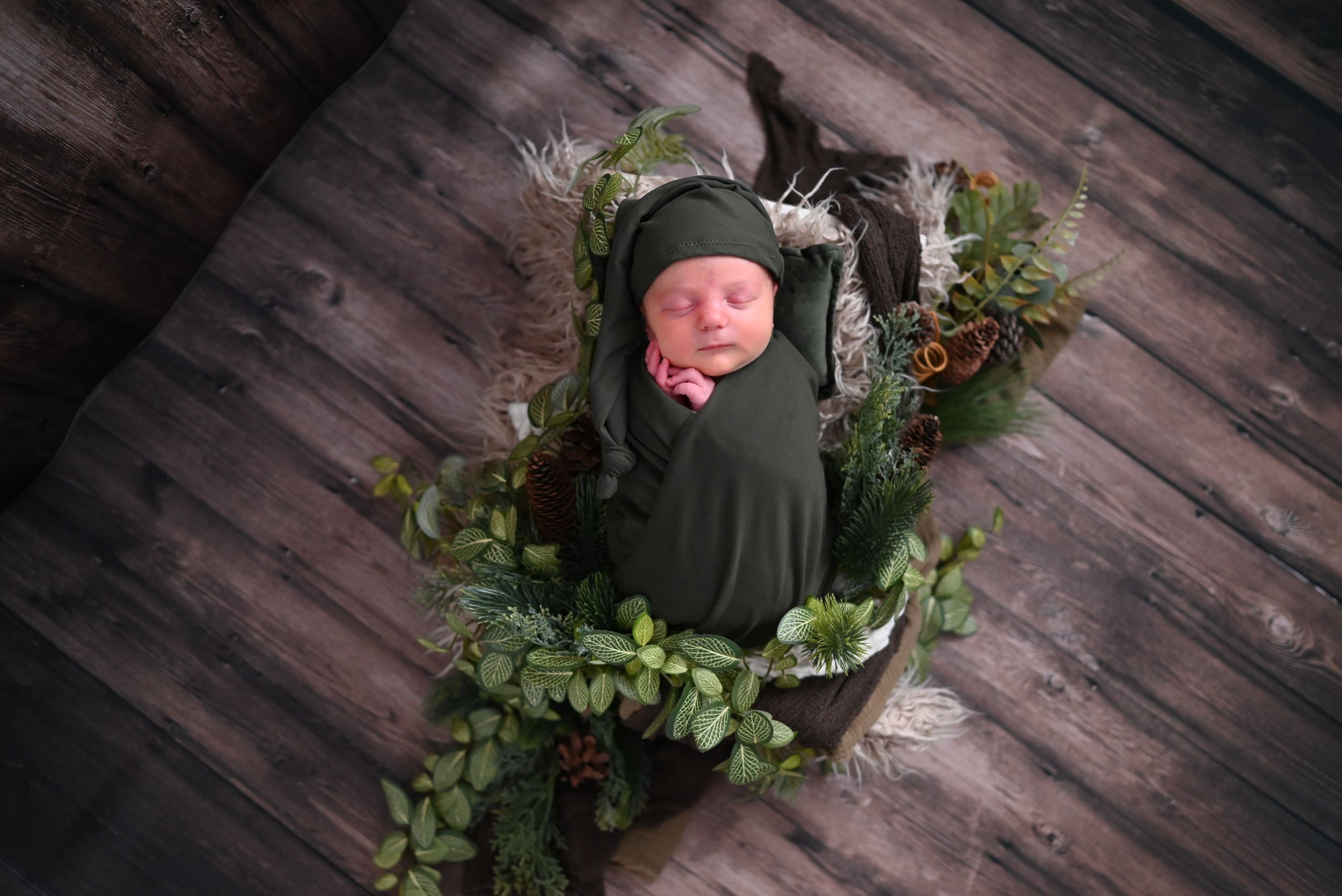 A rustic wooden wreath decorated with fresh greenery, berries, and pinecones hangs on a dark wood plank wall.