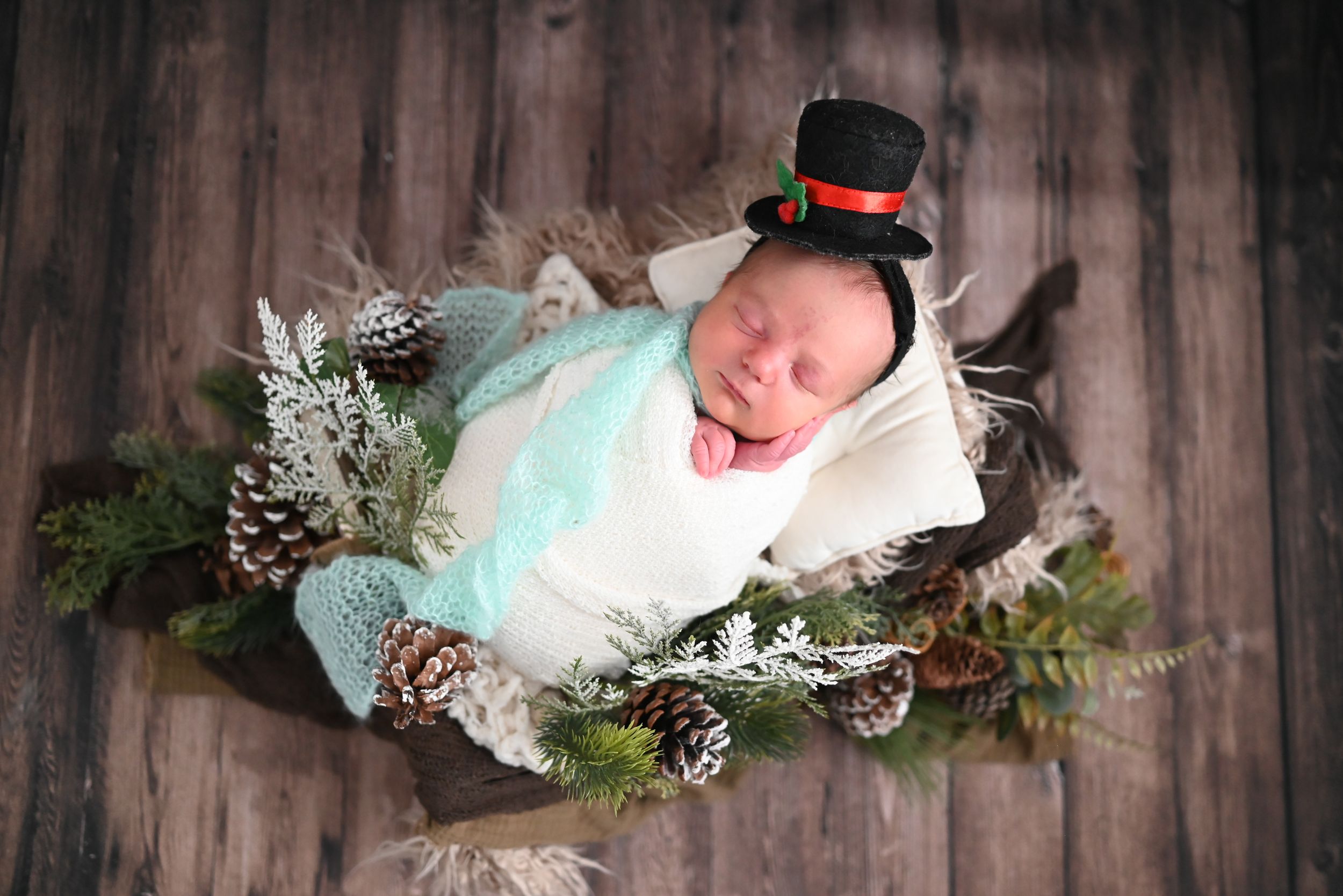 Four close-up photos of a newborn baby in white swaddle blankets with winter holiday decorations and pine branches.