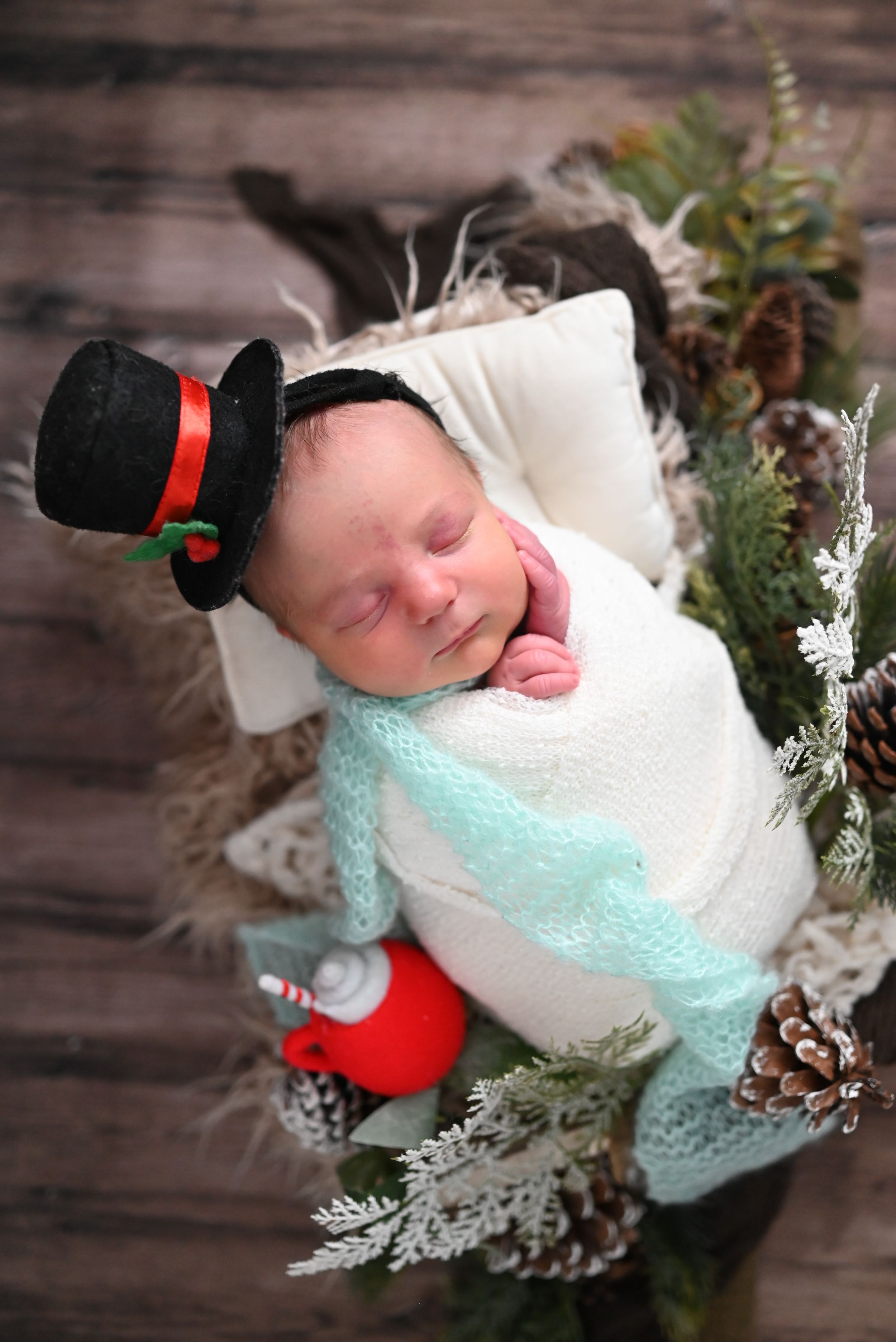 Sleeping newborn wrapped in mint and white swaddle with winter holiday decorations and snowflakes.