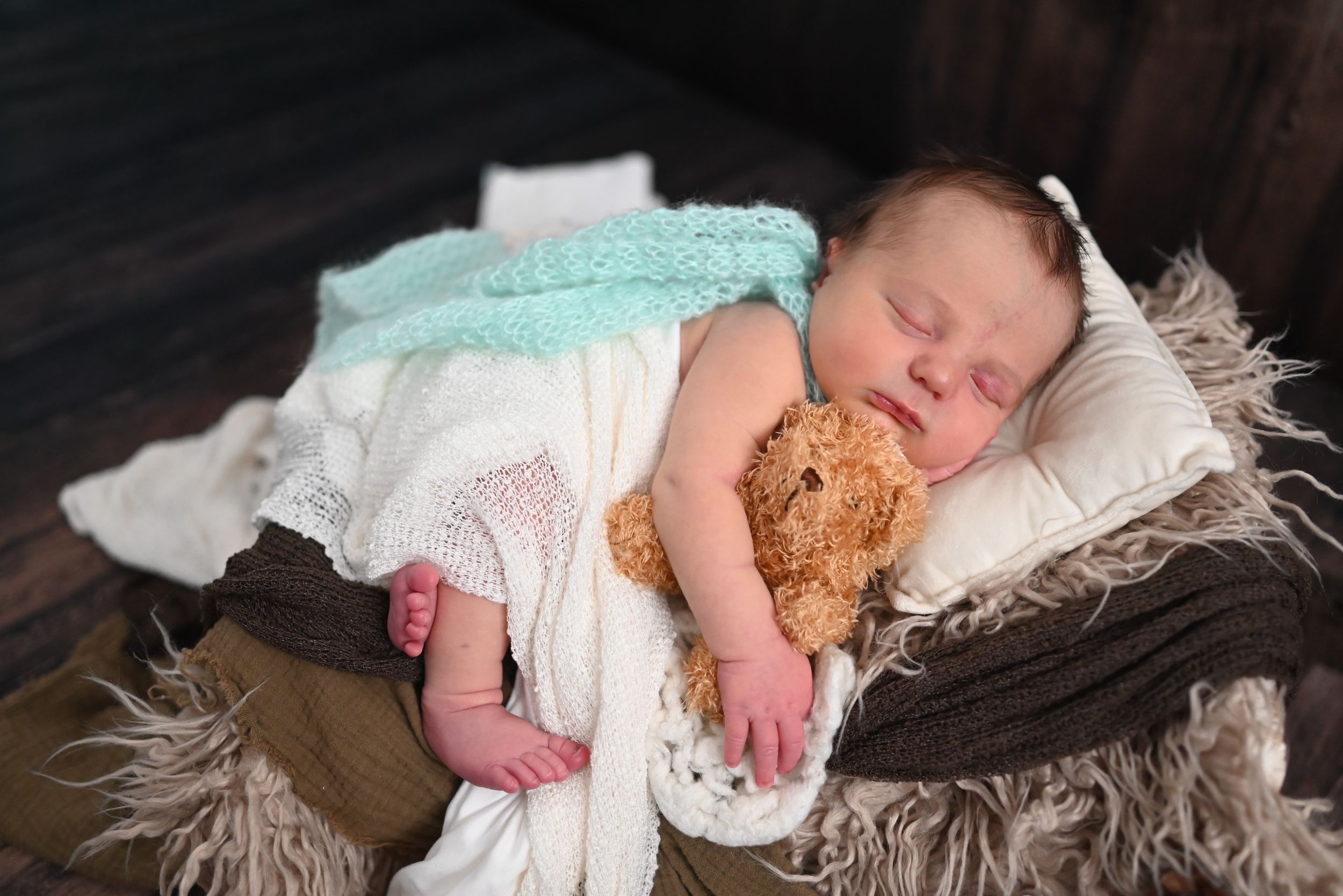 A baby rests peacefully on a textured blanket with winter-themed decorations and pinecones nearby.
