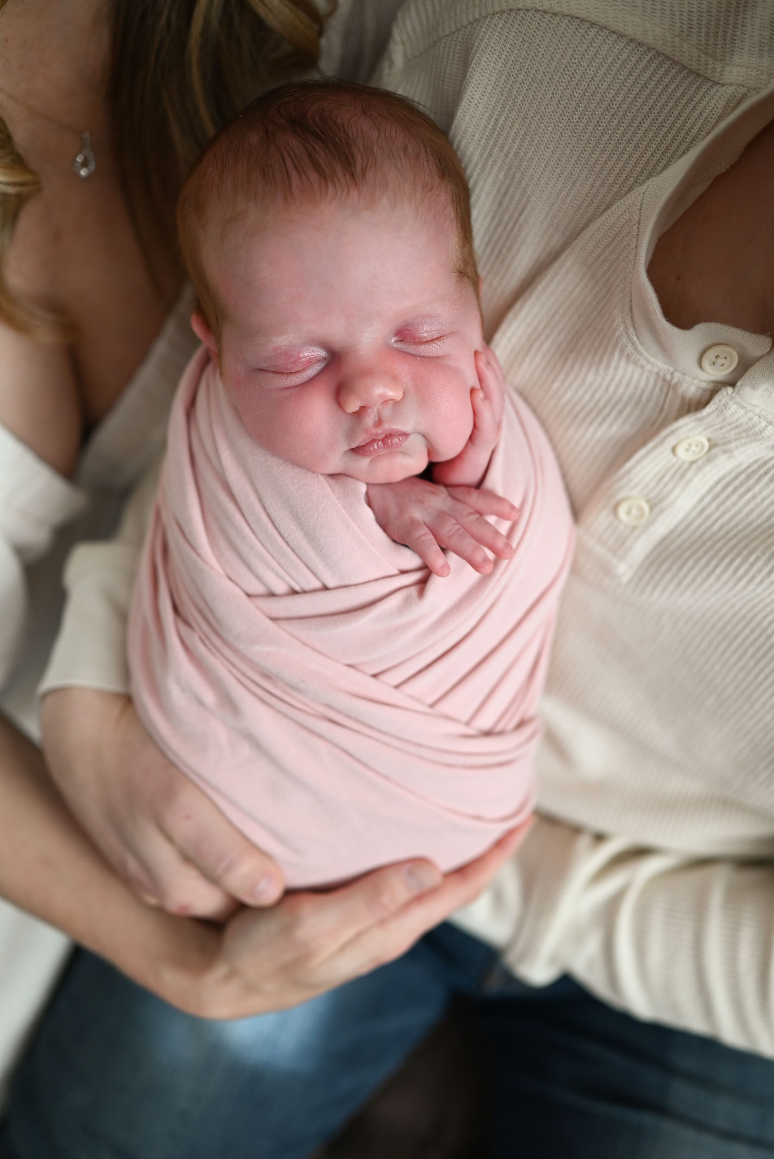 Newborn baby swaddled in pink wrap sleeping peacefully in mother's arms.
