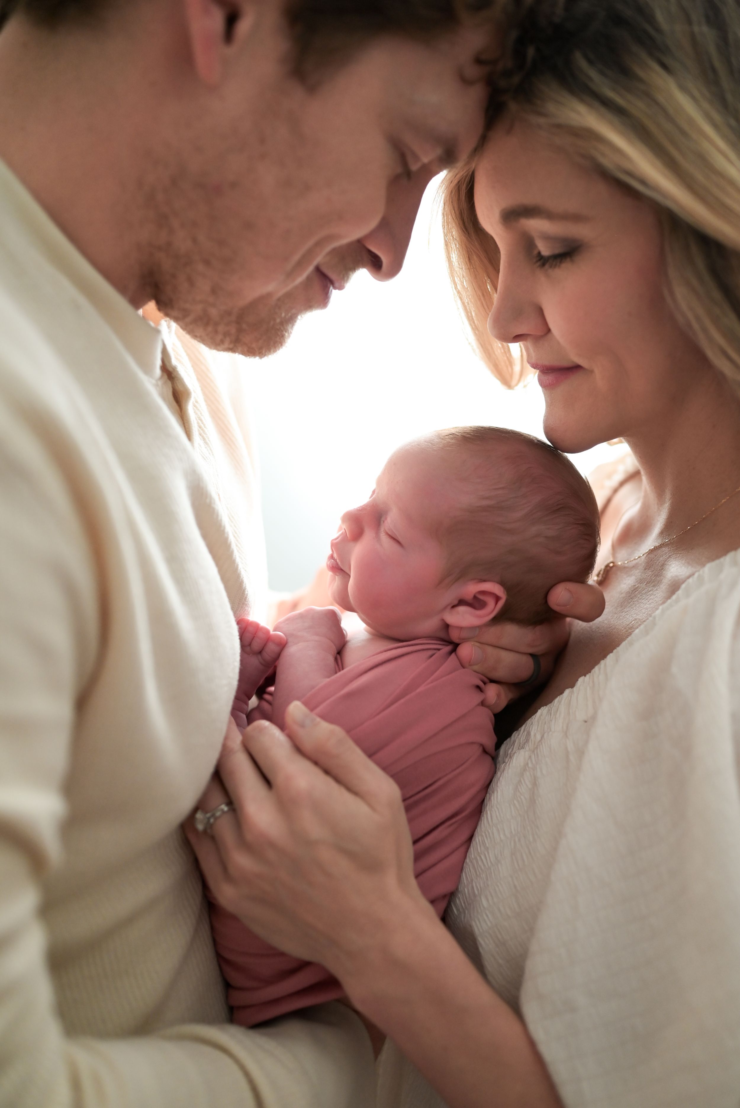 New parents tenderly hold their newborn baby wrapped in a pink swaddle, sharing an intimate family moment.