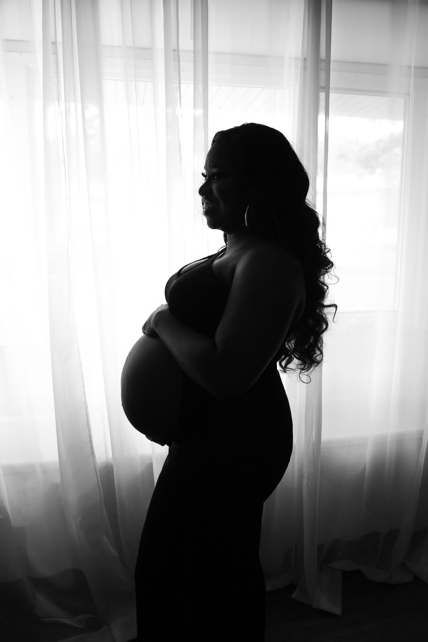 Black and white silhouette series showing a couple embracing in front of sheer curtains with natural light.