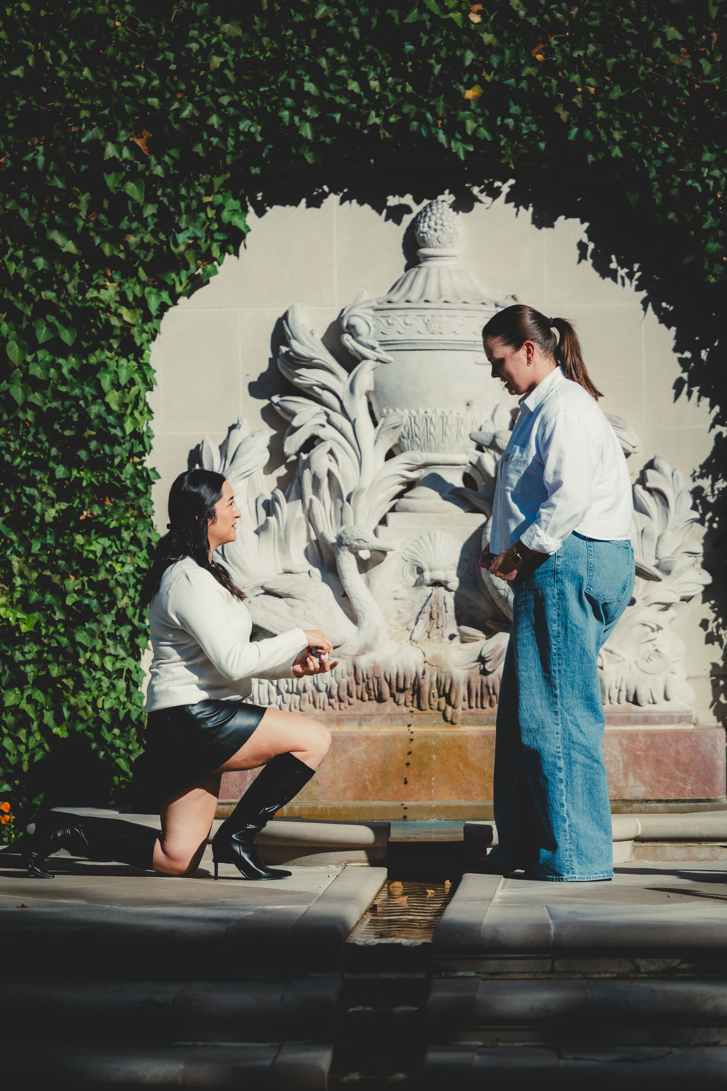 A romantic proposal scene unfolds on a sunny day against a decorative stone wall background at the Hillwood Estate