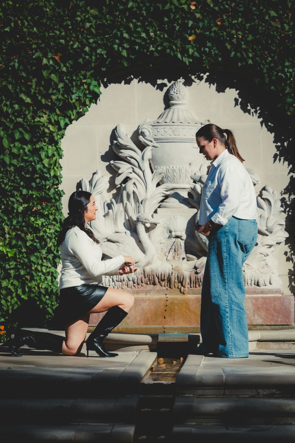 A romantic proposal scene unfolds on a sunny day against a decorative stone wall background at the Hillwood Estate