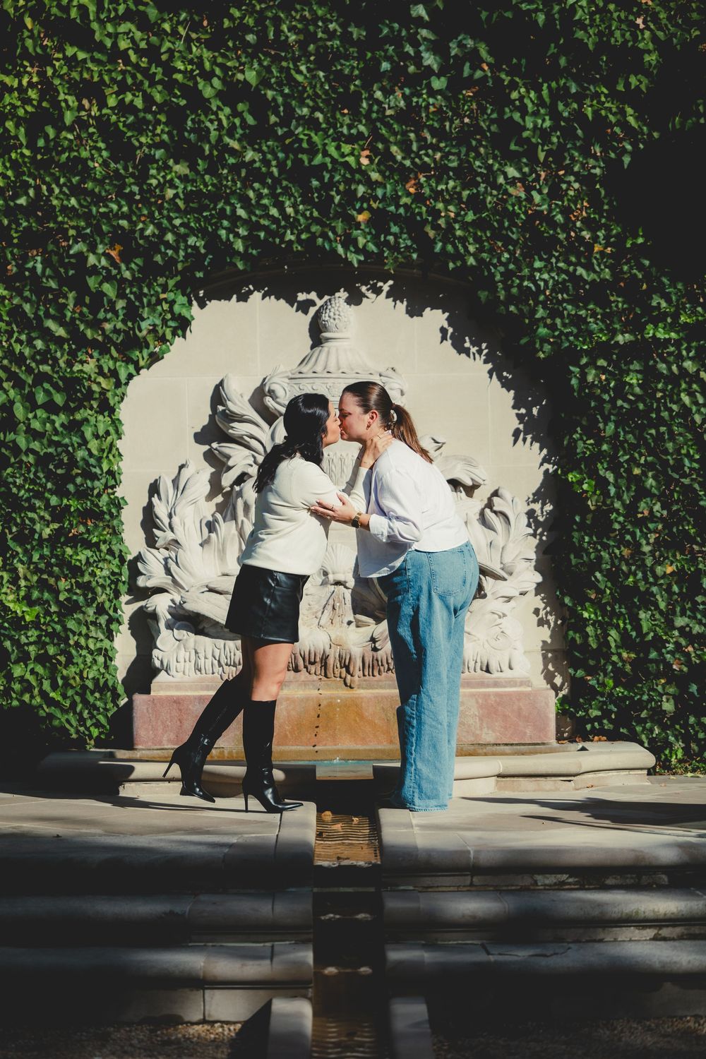 A couple poses playfully against an ivy-covered wall with artistic murals at Hillwood Estate gardens