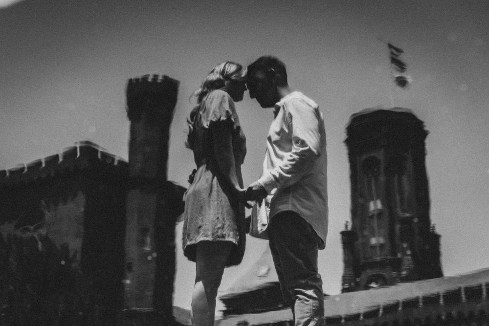 A romantic black and white silhouette of a couple embracing on a rooftop with gothic architecture in the background.