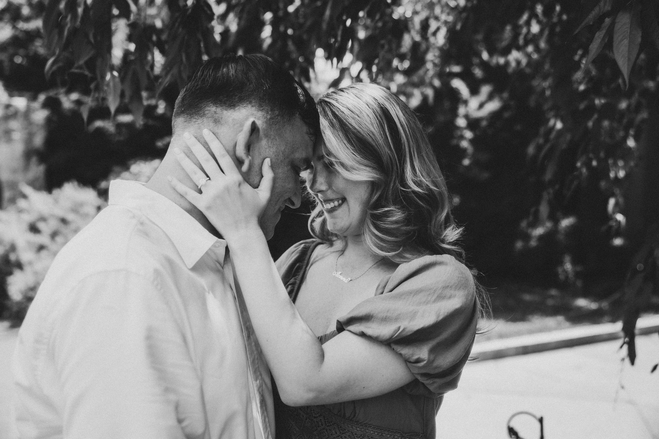Black and white romantic photo of a tender moment between a couple sharing an intimate embrace outdoors.
