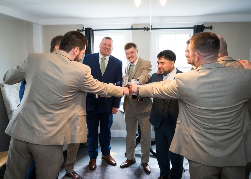 Groomsmen in tan suits huddle together in a celebratory circle before a wedding ceremony.
