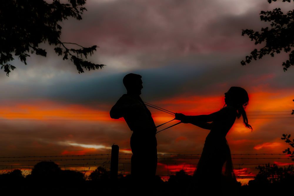 Silhouettes of people fishing at sunset with vibrant orange and red sky reflecting on calm waters.