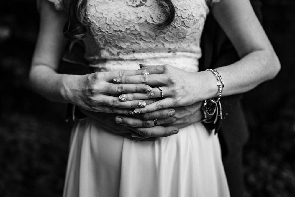 Close-up of hands resting on white wedding dress fabric against dark background.