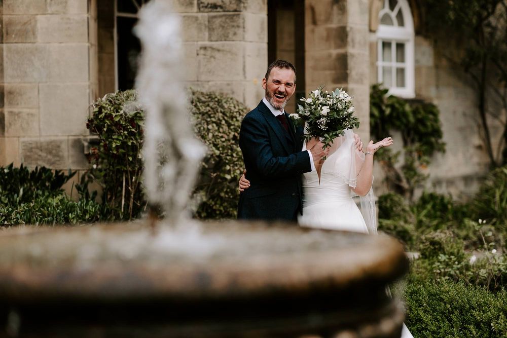 A couple walks together on the grounds of an elegant stone building during a wedding celebration.