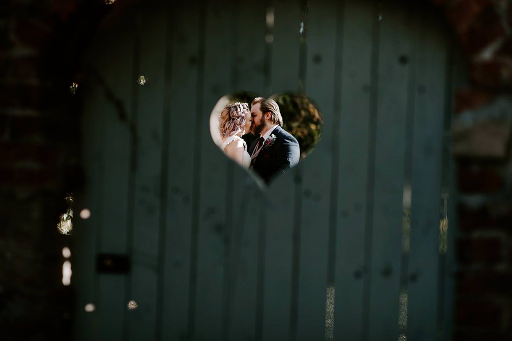 A creative wedding photo captured through a heart-shaped opening showing a couple in an embrace.