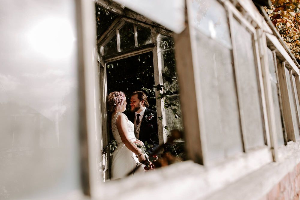 A couple shares an intimate moment in a window frame while confetti falls around them during their wedding celebration.