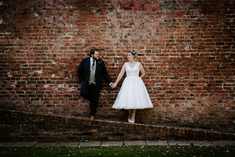 Wedding couple poses against rustic brick wall in black and white photography series.