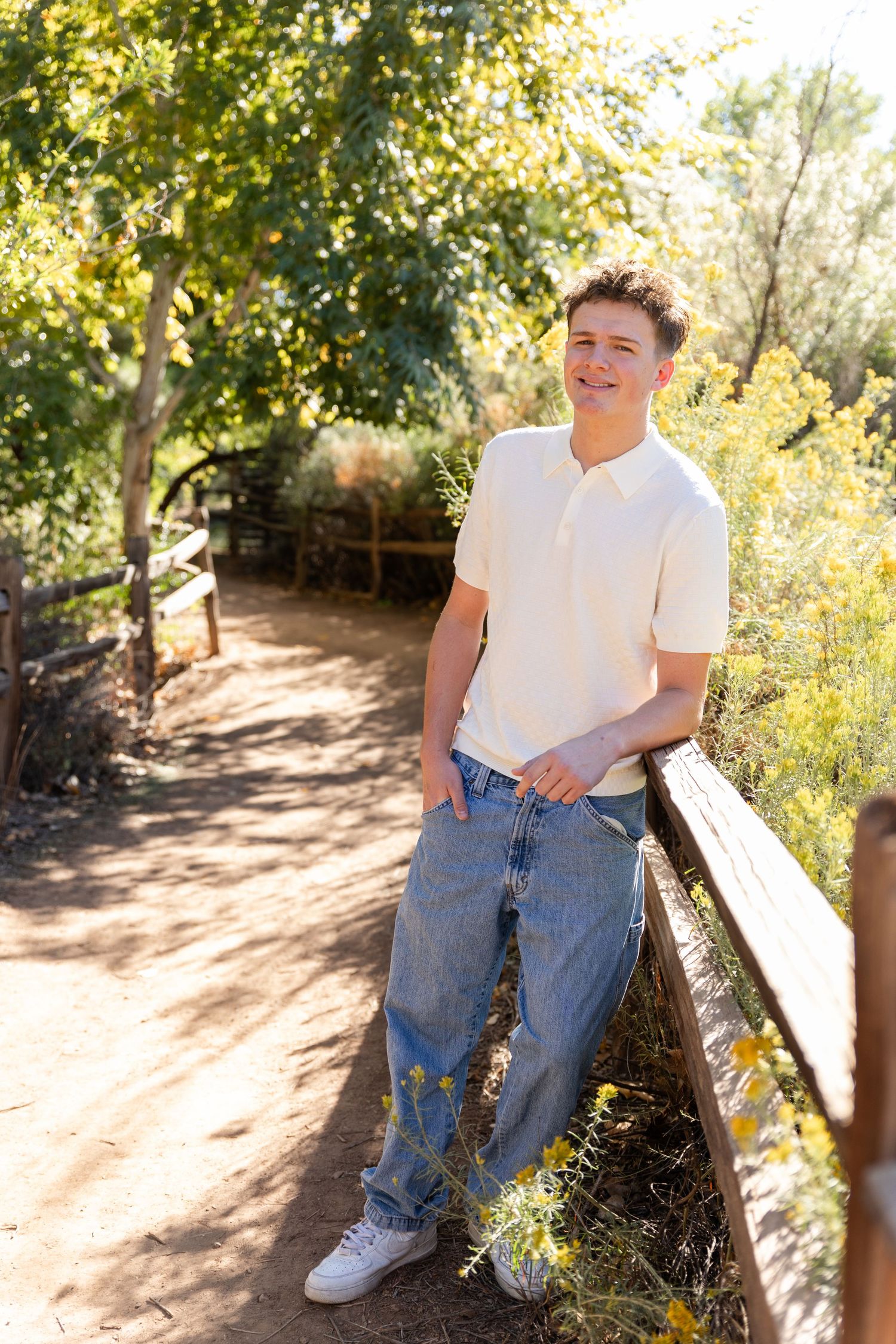 gorgeous Tonaquint Park in southern utah a senior boy leaning against the fence hands in pockets smiling at camera in wooded area