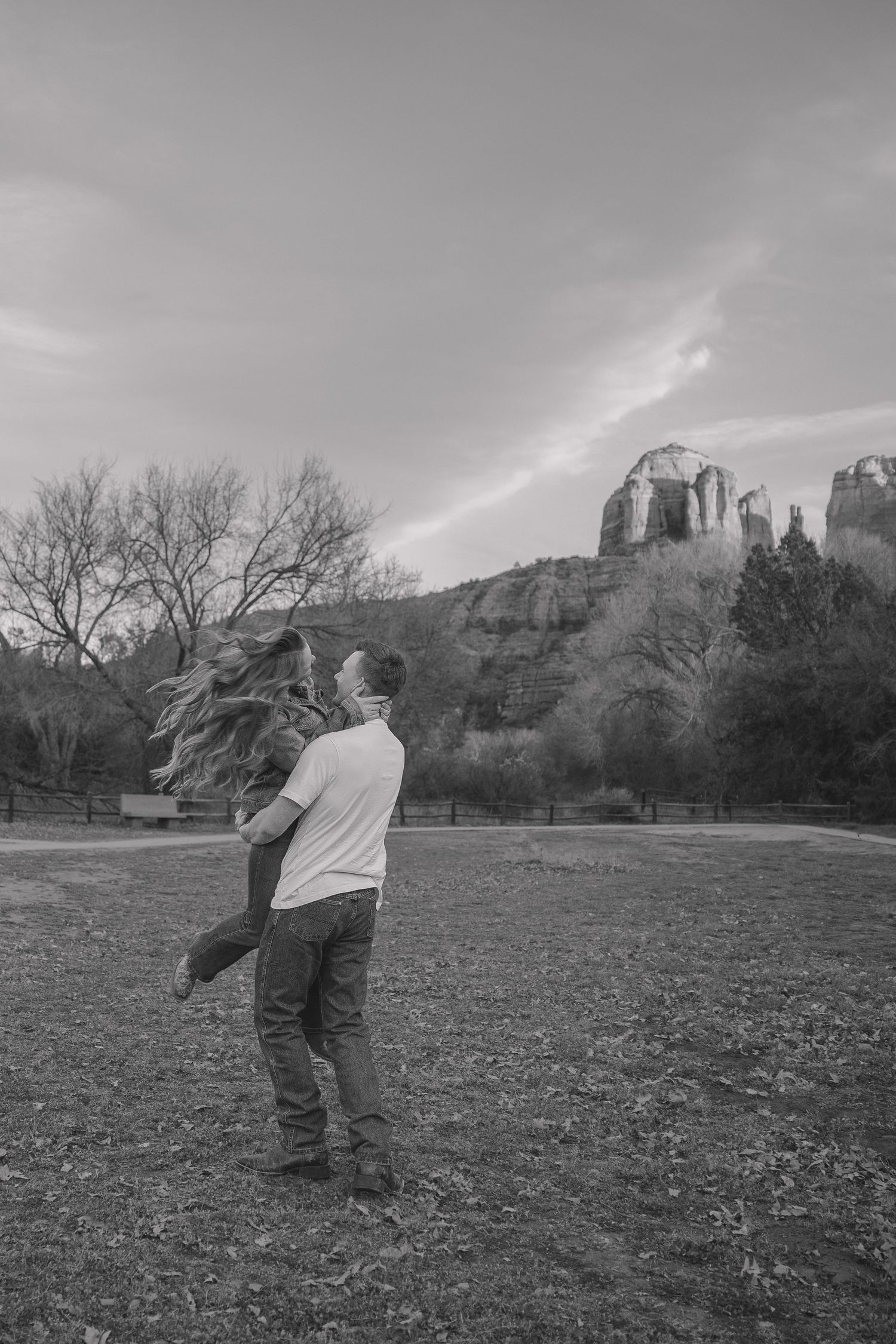 Black and white photo of a couple dancing in a field with majestic rock formations in the distance.