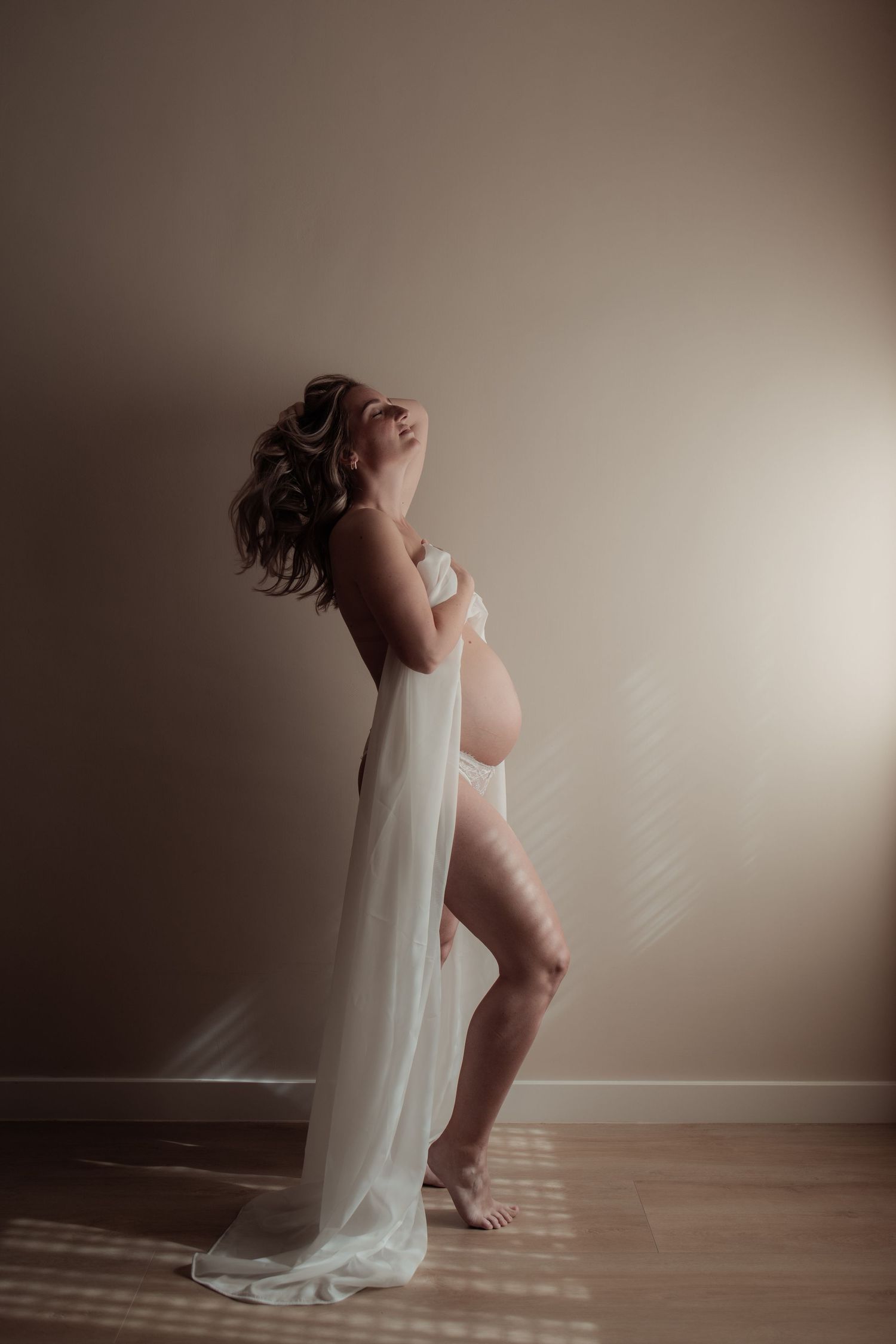 A maternity photo series showing a pregnant woman in a flowing beige dress against a natural outdoor backdrop.