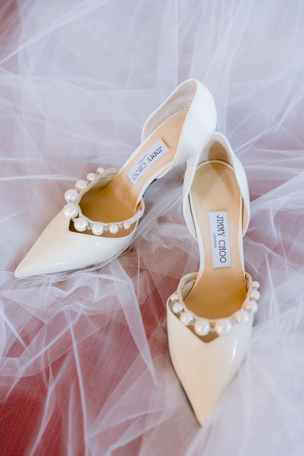 Elegant white Jimmy Choo bridal shoes with pearl embellishments displayed on delicate tulle fabric.