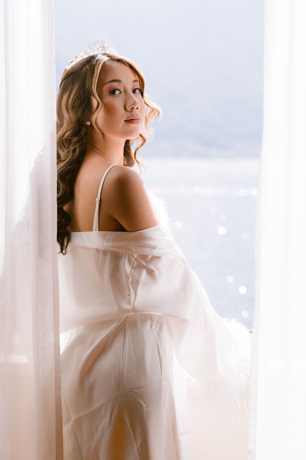 Intimate boudoir photography featuring delicate white fabric and natural window lighting creating an elegant mood.
