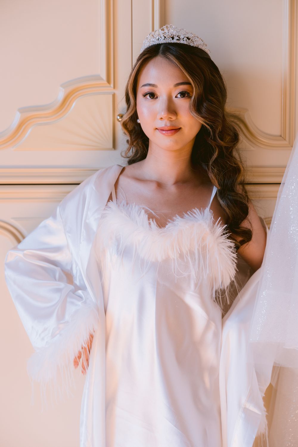 Ethereal white feathered dress with flowing sleeves photographed against elegant cream-colored wall panels.