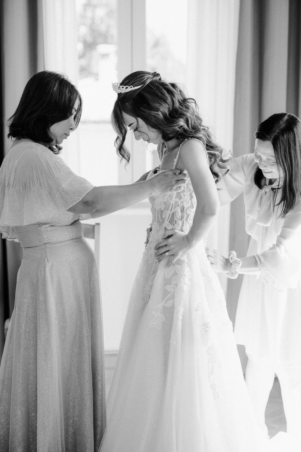 A row of bridesmaids in soft pastel dresses stand together in a light-filled room creating an elegant silhouette.