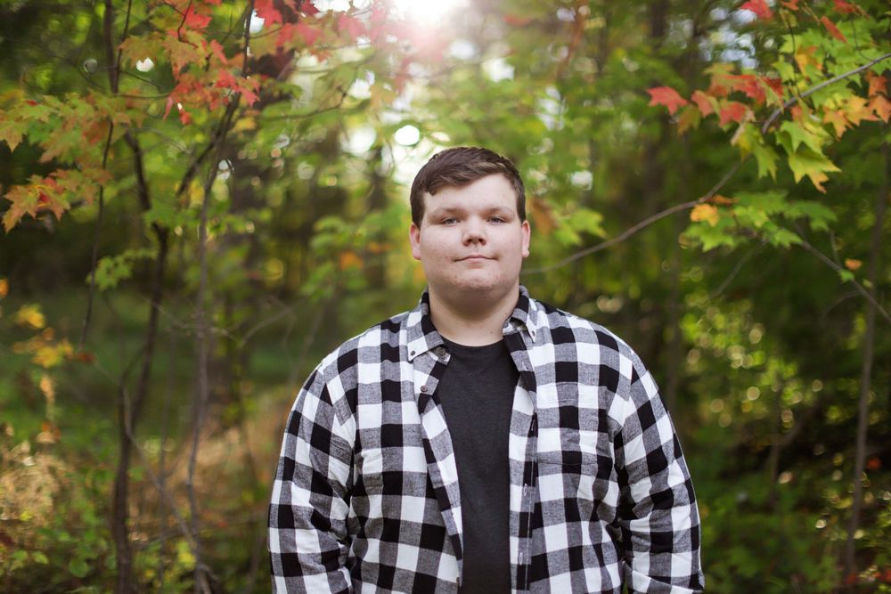 A fall portrait session in a wooded area with colorful autumn foliage and natural sunlight filtering through trees.
