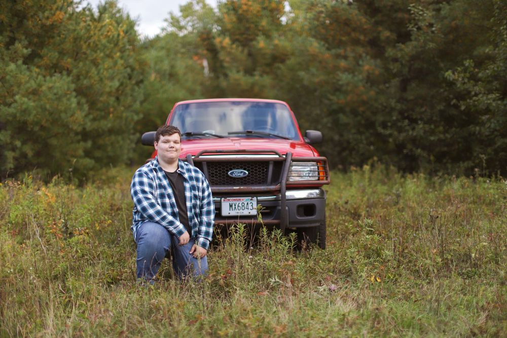 Red pickup truck parked in a grassy field during autumn with trees and fall colors in the background.