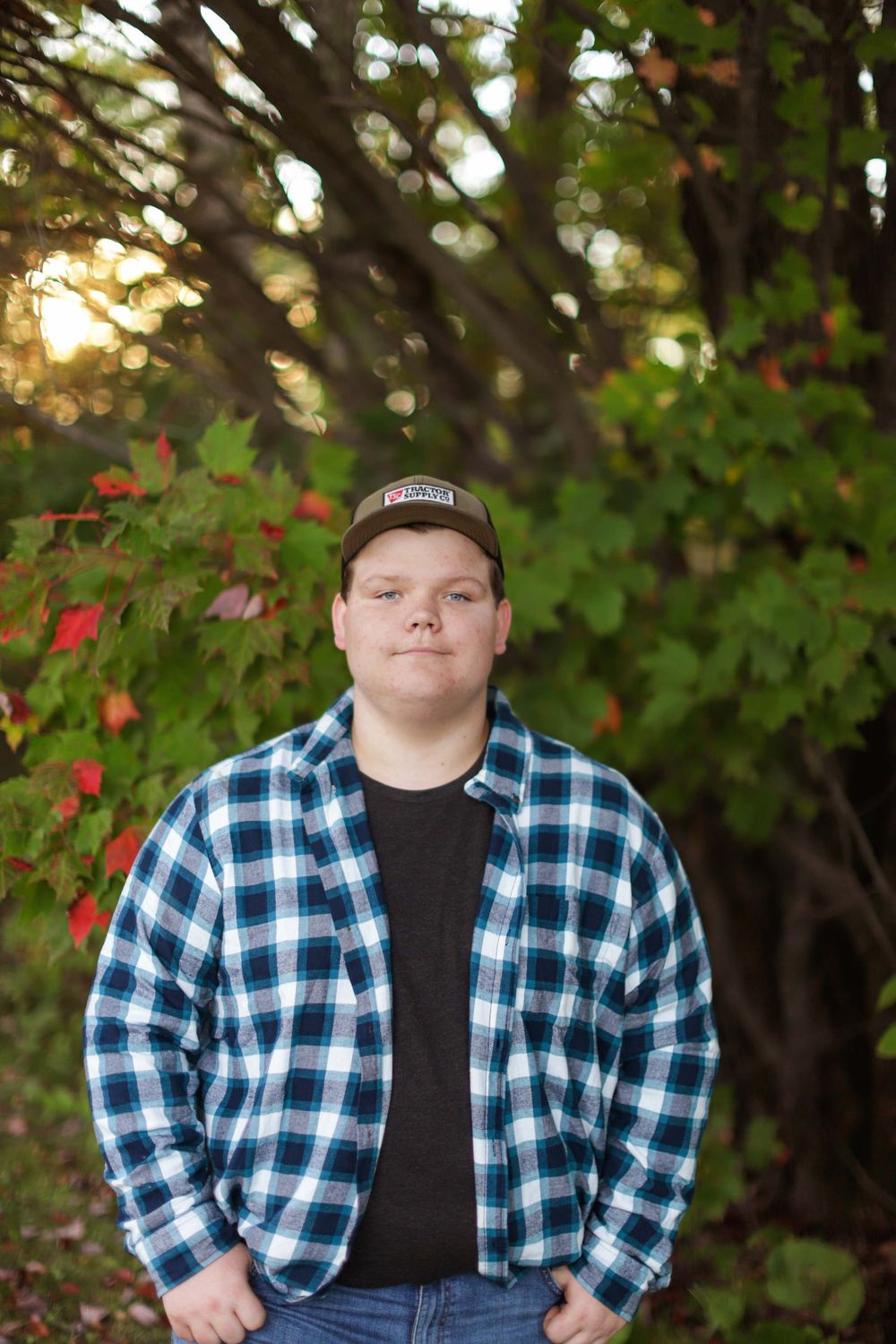 Portrait of someone wearing a blue plaid flannel shirt and baseball cap in an autumn outdoor setting.