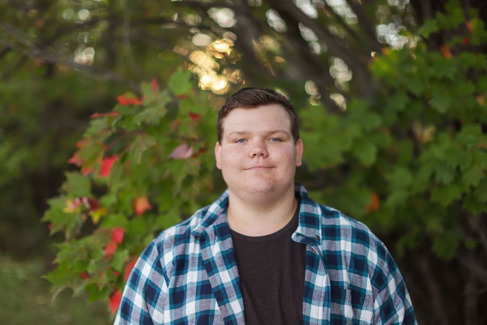 Casual outdoor portrait with person in plaid flannel shirt against autumn foliage and natural lighting.