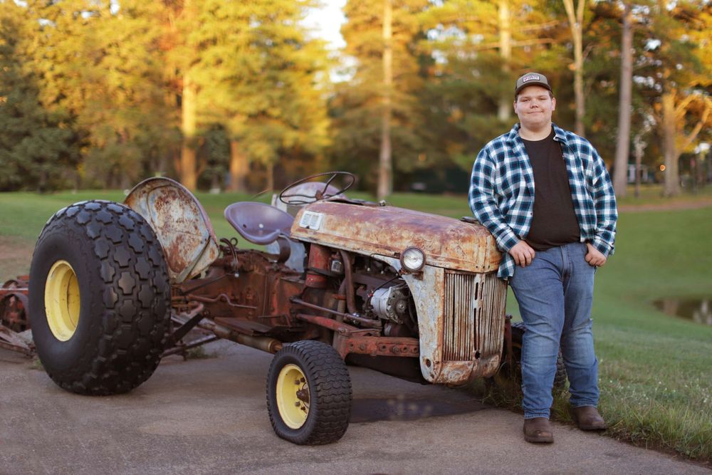 Vintage farm tractor parts and rusty equipment displayed on grassy lawn during autumn season.