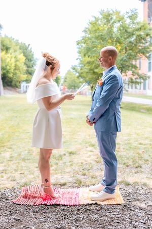 A couple in wedding attire shares a playful moment on a grassy hill, with the bride in white and groom in blue suit.
