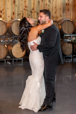 Couple performs romantic dip dance move during wedding reception in rustic winery barrel room.