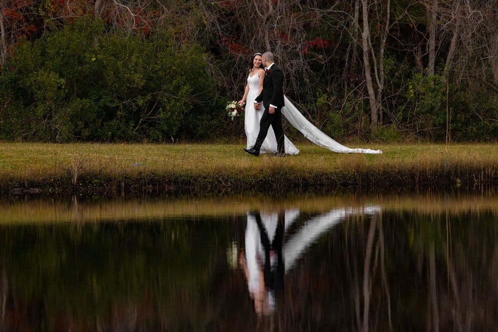 Elegant outdoor wedding ceremony taking place beside a serene lake with trees in the background.